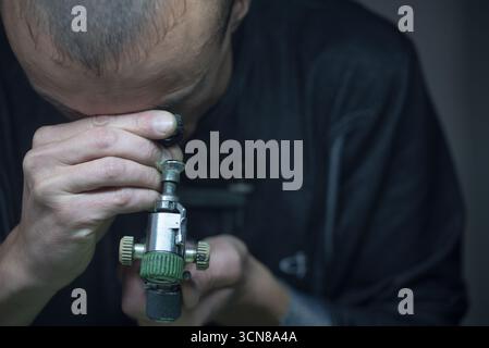 A man is looking through a magnifying glass. He is wearing a black shirt and has a bald head Stock Photo
