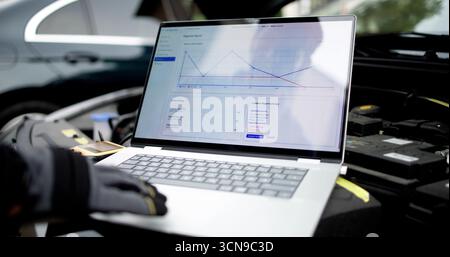 Experienced Mechanic Using Laptop To Diagnose Car Engine In Garage. Potential Professions: Mechanic, Technician Stock Photo