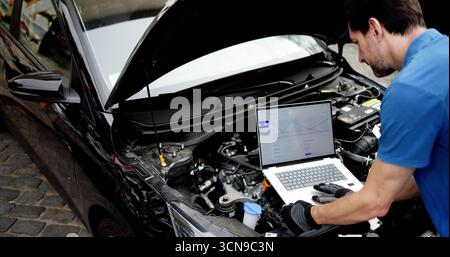 Skilled Mechanic Using Laptop To Diagnose Car Issues In Garage. Doctor Examining Patient Stock Photo