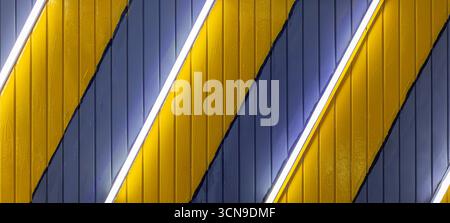 Vibrant indoor wall features diagonal yellow and dark blue stripes, illuminated by light strips. The modern design creates a bold geometric aesthetic Stock Photo