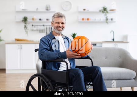 Man practicing basketball while seated in wheelchair in modern home environment Stock Photo