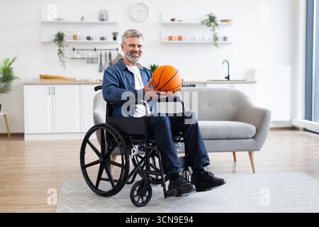 Man practicing basketball while seated in wheelchair in modern home environment Stock Photo