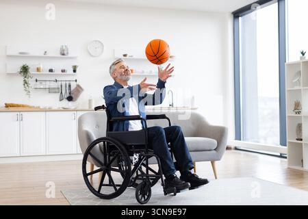 Man in wheelchair practicing basketball in modern living room setting Stock Photo