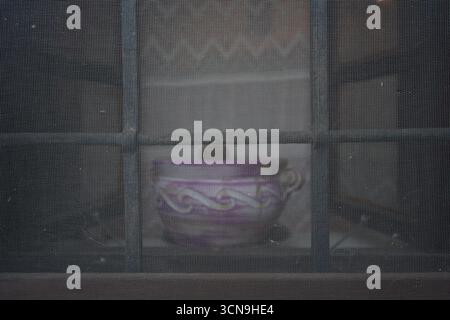 A close-up, artistic shot of a small purple pot with an ornate design, viewed through a fine mesh screen. Stock Photo