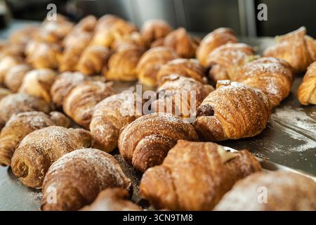 Many golden-brown croissants are resting on a counter, freshly baked and dusted with a delicate layer of powdered sugar, highlighting the concept of d Stock Photo