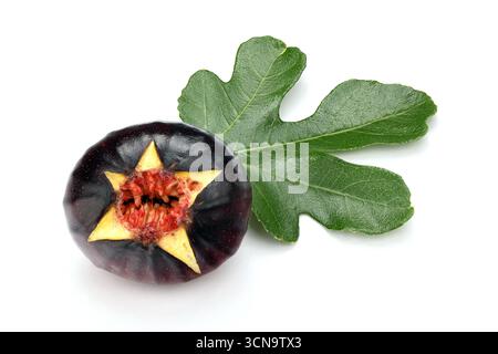 A black star fruit with a green leaf on top. The fruit is cut in half and the leaf is next to it Stock Photo
