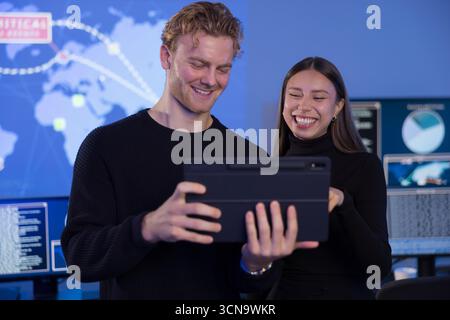 Team collaboration analyzing data on a tablet in a high-tech SOC environment Stock Photo