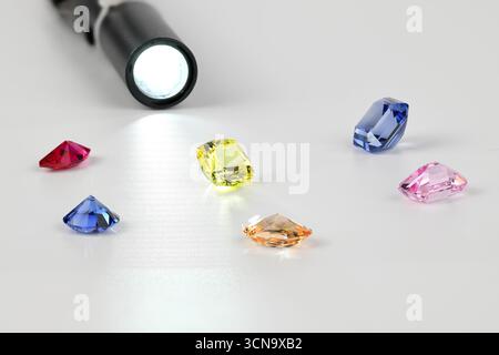 A flashlight is shining on a table with a variety of colored gems. The gems are arranged in a way that highlights their different colors and shapes. C Stock Photo