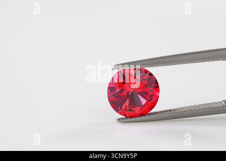 A red gemstone is being held up by a metal tool. The gemstone is shiny and has a beautiful red color Stock Photo