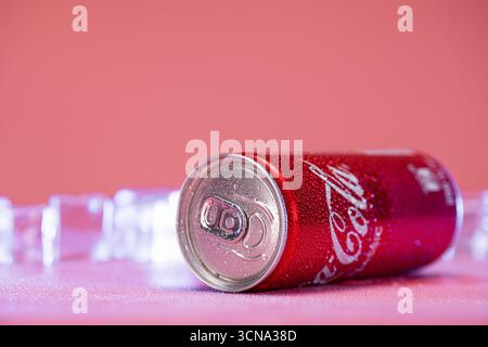 A can of Coca-Cola is sitting on a table with ice cubes. The can is partially opened and has a shiny, metallic appearance. The ice cubes are scattered Stock Photo