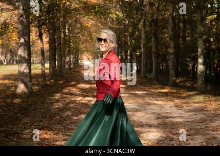 A happy sixty-year-old gray-haired woman strolls in the gardens of Versailles Stock Photo