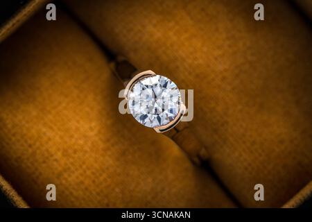 A gold and diamond ring is displayed in a box. The ring is a beautiful, sparkling diamond that is set in a gold band. The box is made of a warm, yello Stock Photo