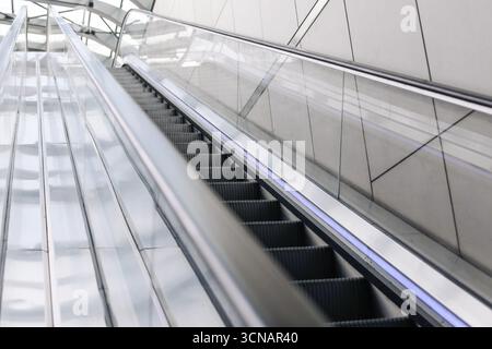 Escalator in modern building interior. Moving staircase in empty hall. Futuristic design and transportation detail. Architecture and urban lifestyle. Stock Photo