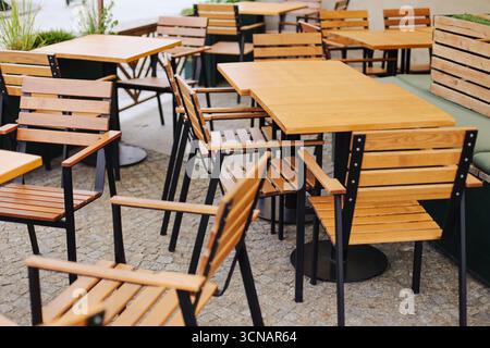 Outdoor cafe terrace. Wooden tables with chairs. Empty seating area in restaurant garden. Urban leisure place with modern design. Relaxing space. Stock Photo