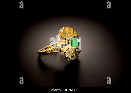 A gold emerald ring with a green stone in the center. The ring is very ornate and has a diamond on the top Stock Photo