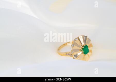 A gold and emerald ring with a diamond in the center. The ring is on a white background Stock Photo