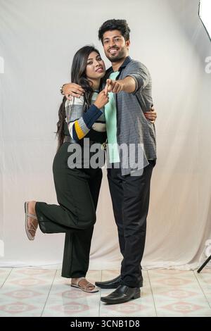 A young couple striking a playful and joyful pose. Playful Couple Hugging and Pointing - Studio Portrait Stock Photo