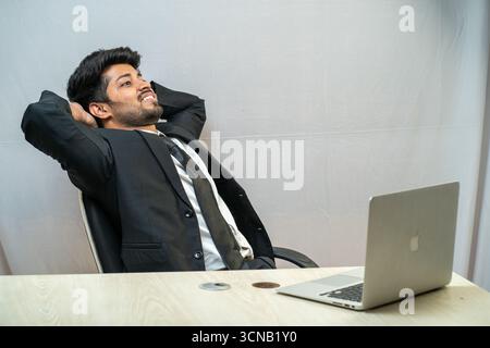 A young businessman sitting in an office chair, relaxing with a laptop. Stock Photo