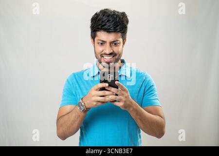 A young man smiling and happily using his mobile phone. Stock Photo