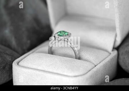 A beautiful green and white diamond ring is placed inside a white box. The ring is adorned with diamonds and is set in a white box. The box is placed Stock Photo
