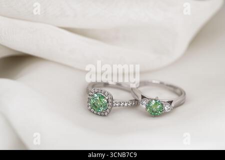 Two green rings are on a white cloth. The rings are made of silver and have a green stone in the middle Stock Photo