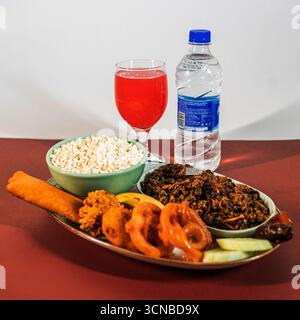 A traditional Iftar platter featuring a bowl of puffed rice, savory fried snacks, a meat or lentil dish, a glass of juice, and a bottle of water. Stock Photo
