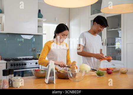 Asian couple chopping vegetables on island in home kitchen with knives and glass salad bowl Stock Photo