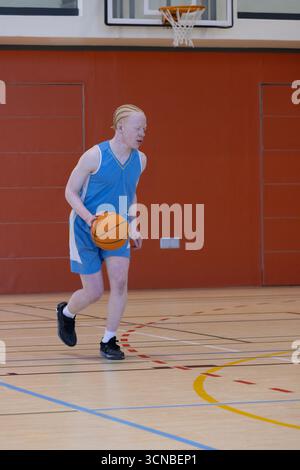 Orange basketball bouncing across wooden gym court marked with colored lines under padded wall Stock Photo