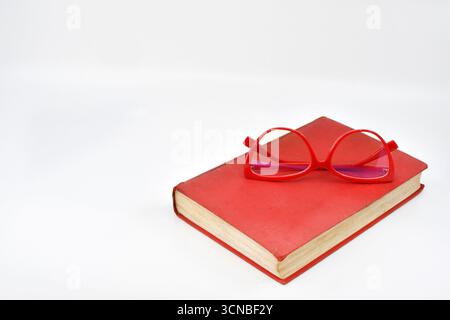 Pair of women's reading glasses on the cover of a book isolated on a plain white background. Copy space. Stock Photo