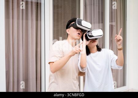 A casual couple wears VR headsets, exploring immersive technology together at home Stock Photo