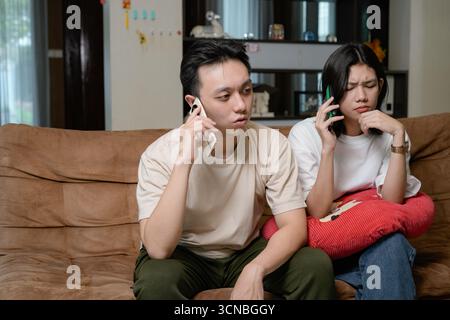 casual asian couple relaxing on a couch looking at phones in a cozy living room Stock Photo
