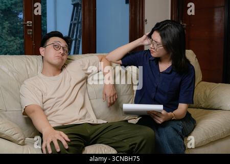 A problem man relaxes on a beige sofa while a woman, wearing glasses, writes in a notebook and reviews papers. psychotheraphy concept Stock Photo