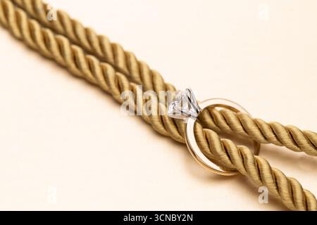 A gold rope with a diamond ring on it. The rope is tied to a table Stock Photo