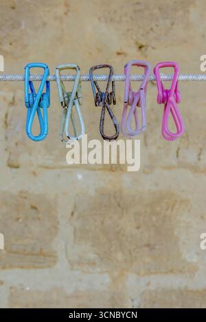 Old weathered colorful metal clothespin covered in plastic, hanging from a cord against an adobe wall, in a farm house in the eastern Andean mountains Stock Photo
