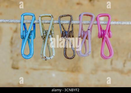 Old weathered colorful metal clothespin covered in plastic, hanging from a cord against an adobe wall, in a farm house in the eastern Andean mountains Stock Photo