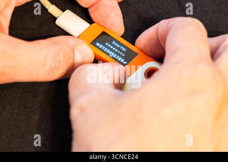 Adult man with light skin using orange hardware Bitcoin wallet displaying PIN code. Stock Photo
