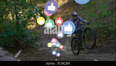 Doing wheelie man wearing helmet, gloves mountain biking on wooded trail, floating thumbs-up icons Stock Photo
