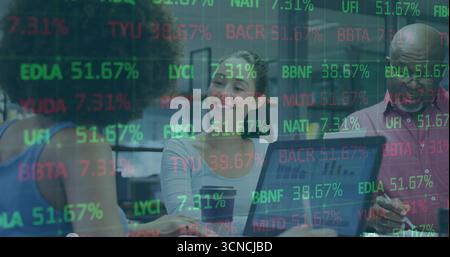 Reviewing three professionals analyzing financial data at conference table, with stock tickers Stock Photo