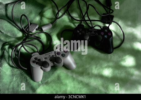 19  September 2025, Wroclaw Poland. Two PlayStation Dual Shock controllers grey and black version lie on a blanket, illuminated by the morning light. Stock Photo