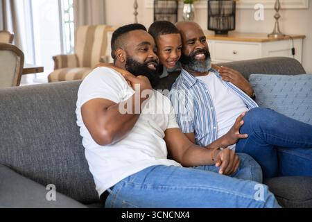 African American family sitting on gray upholstered sofa smiling toward off-frame in living room Stock Photo
