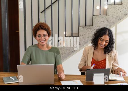 Diverse female colleagues collaborating on report at desk using laptop tablet stylus Stock Photo