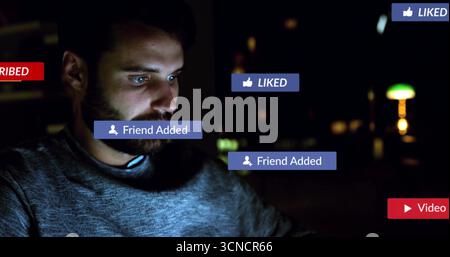Bearded man wearing grey sweater scrolling on computer at desk, with floating social notifications Stock Photo