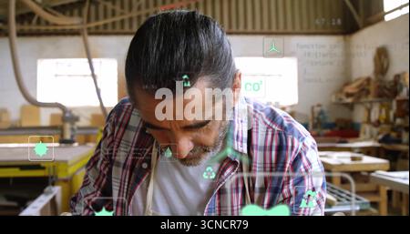 Leaning veteran craftsman scanning digital icons in woodworking workshop, with wooden planks Stock Photo