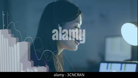 Analyzing charts adult Chinese woman wearing headset at office desk, with glowing monitor overlay Stock Photo