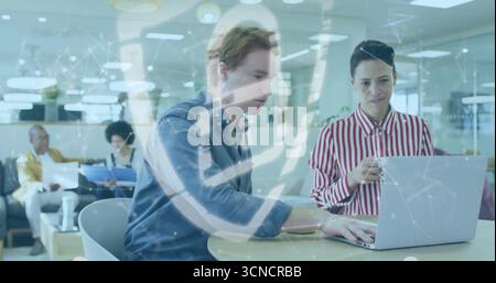 Collaborating two colleagues reviewing report on laptop at table in open office, with coffee mug Stock Photo