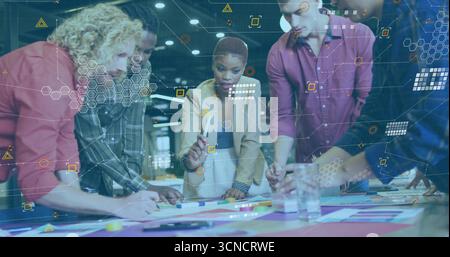 Collaborating coworkers writing on colored papers around table in office under network overlays Stock Photo