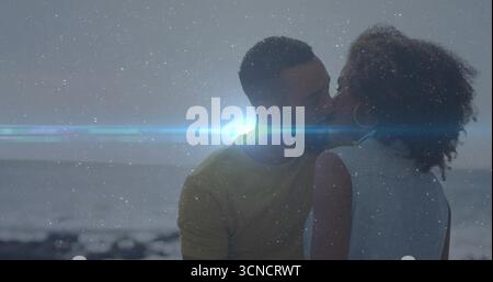 Sharing kiss, romantic couple embracing on rocky shoreline at dusk, with bright lens flare Stock Photo