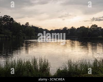 Golden light reflects off the rippling water of a tranquil residential pond with a fountain in Ashburn, Virginia, at sunset. Stock Photo