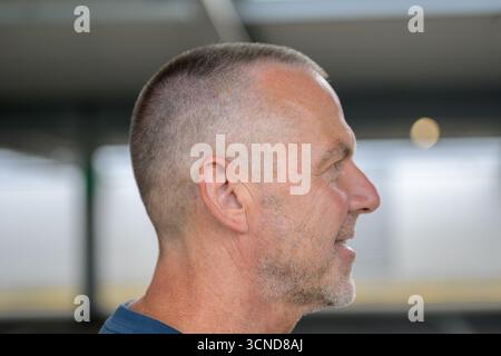 Close-up side profile of a mature man with short-cropped gray hair and stubble, smiling slightly. Stock Photo