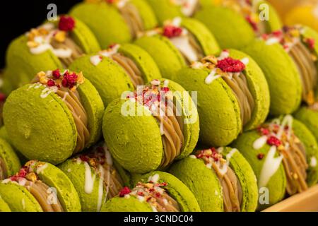 Close-up of green pistachio macarons filled with cream and decorated with dried berries and nuts. Elegant French dessert with vibrant colors Stock Photo